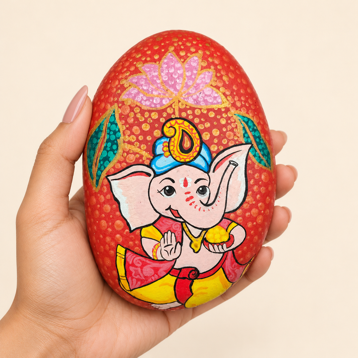 Baal Ganesh: Lotus Play hand-painted natural pebble art, shown in hand for scale