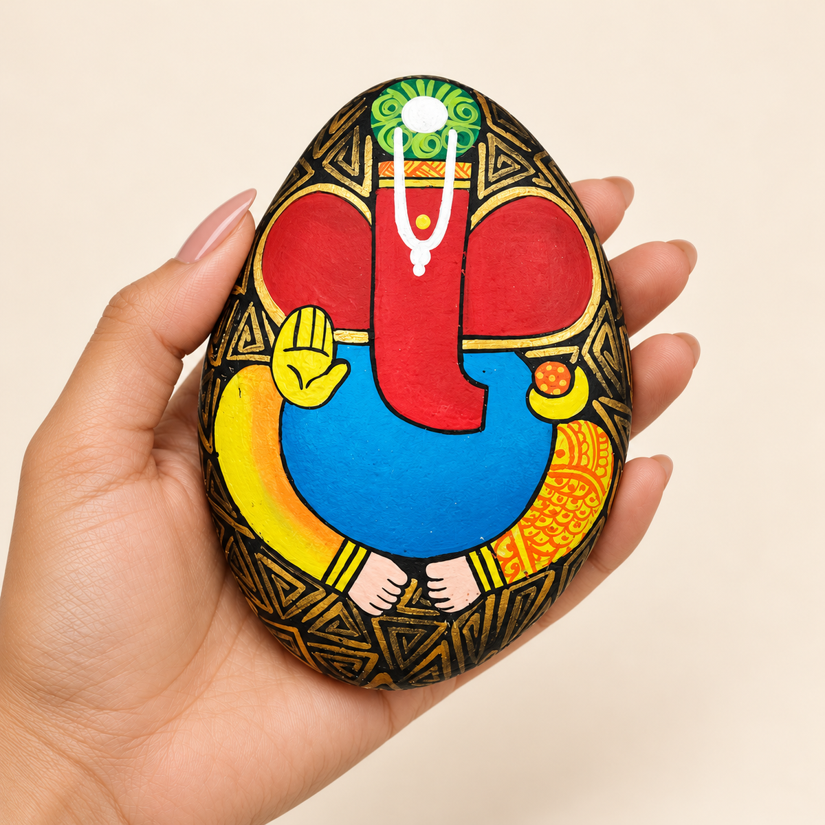 Ganesh: Crimson Blessing hand-painted natural pebble art, shown in hand for scale