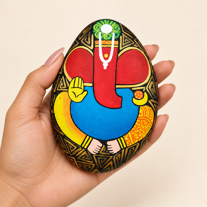 Ganesh: Crimson Blessing hand-painted natural pebble art, shown in hand for scale