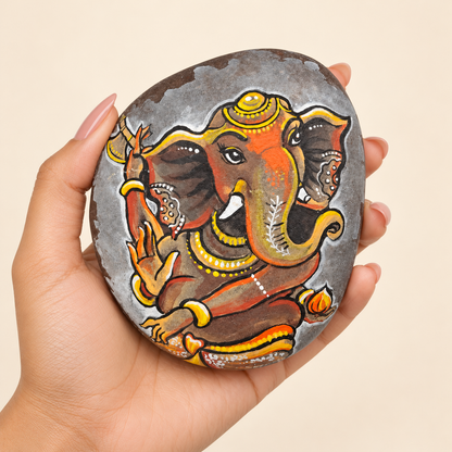 Ganesh: Earthbound Grace hand-painted natural pebble art, shown in hand for scale