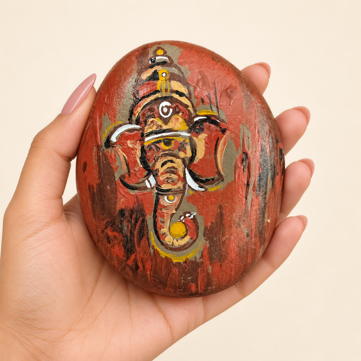 Ganesh: Rustic Devotion hand-painted natural pebble art, shown in hand for scale