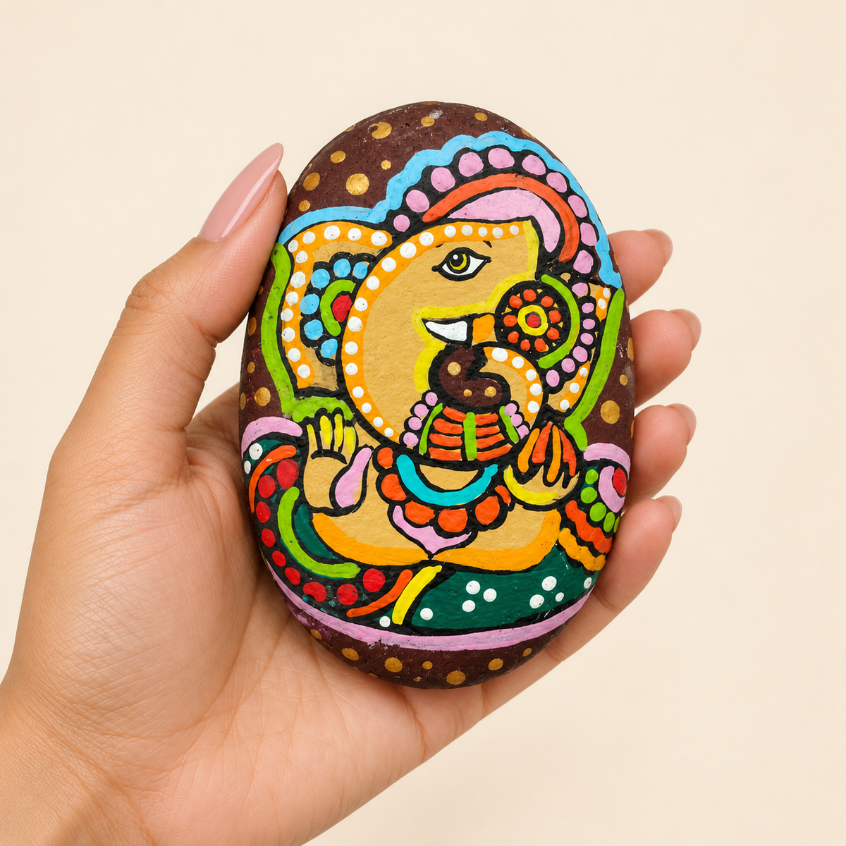 Ganesh: Festive Melody hand-painted natural pebble art, shown in hand for scale