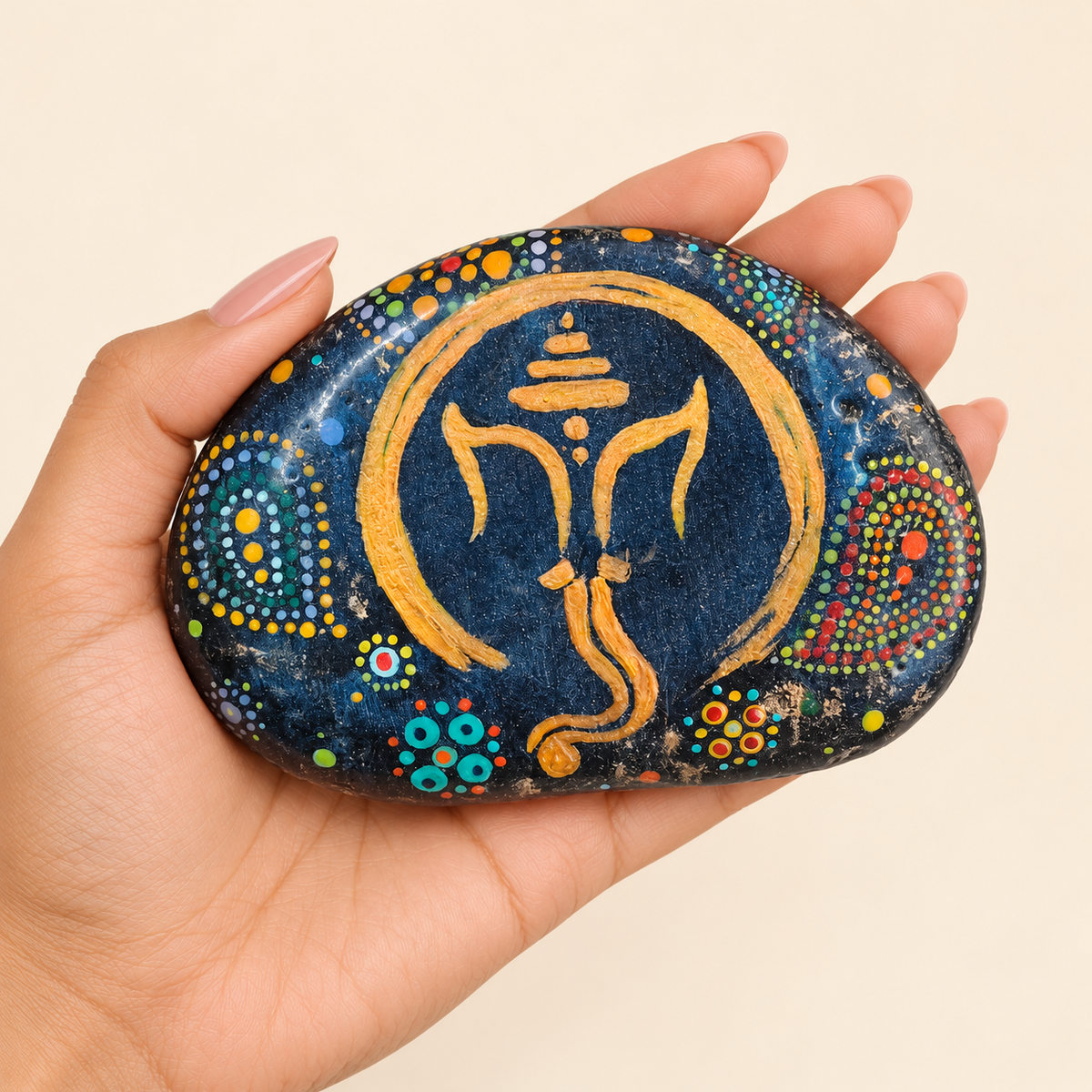 Ganesh: Cosmic Gold hand-painted natural pebble art, shown in hand for scale