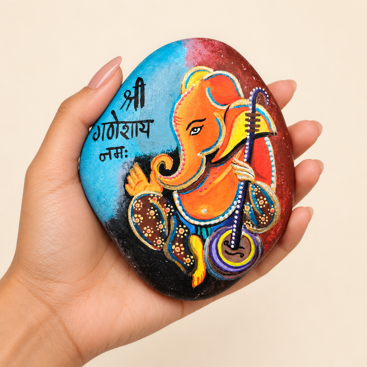 Ganesh: Sacred Melody hand-painted natural pebble art, shown in hand for scale