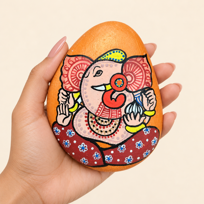 Ganesh: Saffron Smile hand-painted natural pebble art, shown in hand for scale