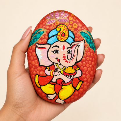 Baal Ganesh: Ruby Joy hand-painted natural pebble art, shown in hand for scale