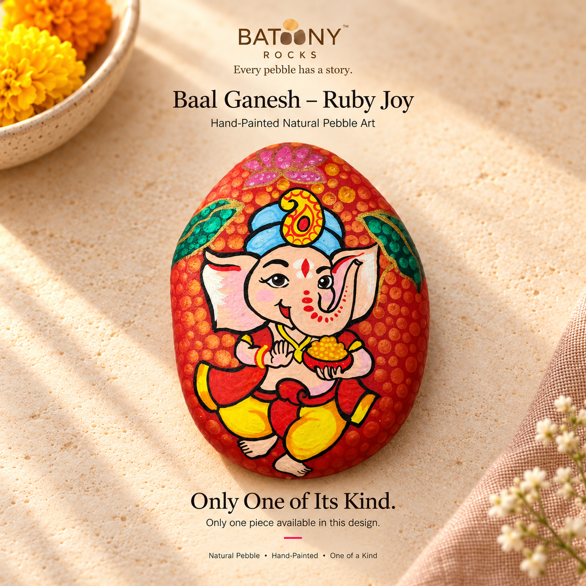 Baal Ganesh: Ruby Joy hand-painted natural pebble art, on a warm stone surface