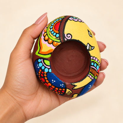 Ganesh: Golden Celebration hand-painted natural pebble tealight holder, shown in hand for scale