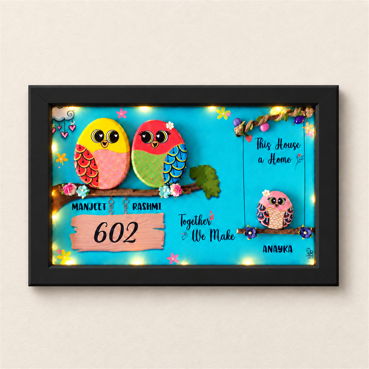Embraced with Love Pebble Art: a colourful family of three birds in a framed artwork, black frame, on a beige background