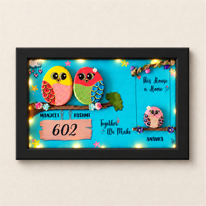 Embraced with Love Pebble Art: a colourful family of three birds in a framed artwork, black frame, on a beige background