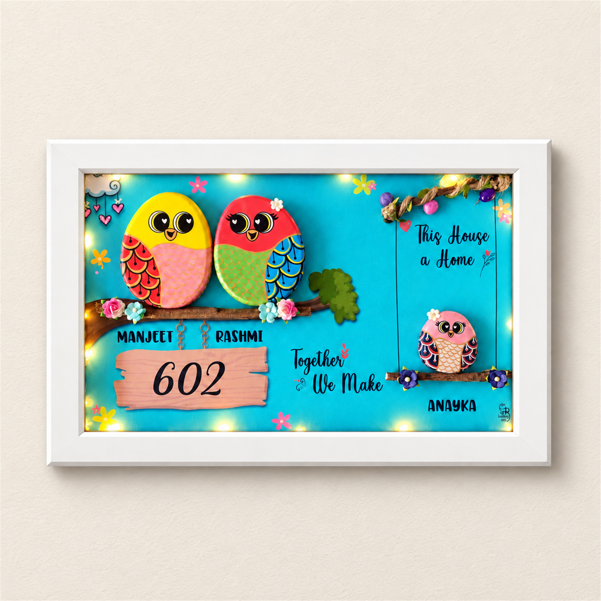 Embraced with Love Pebble Art: a colourful family of three birds in a framed artwork, white frame, on a beige background