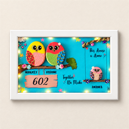 Embraced with Love Pebble Art: a colourful family of three birds in a framed artwork, white frame, on a beige background