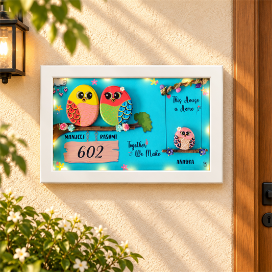 Embraced with Love Pebble Art: a colourful family of three birds in a framed artwork, white frame, in a home setting