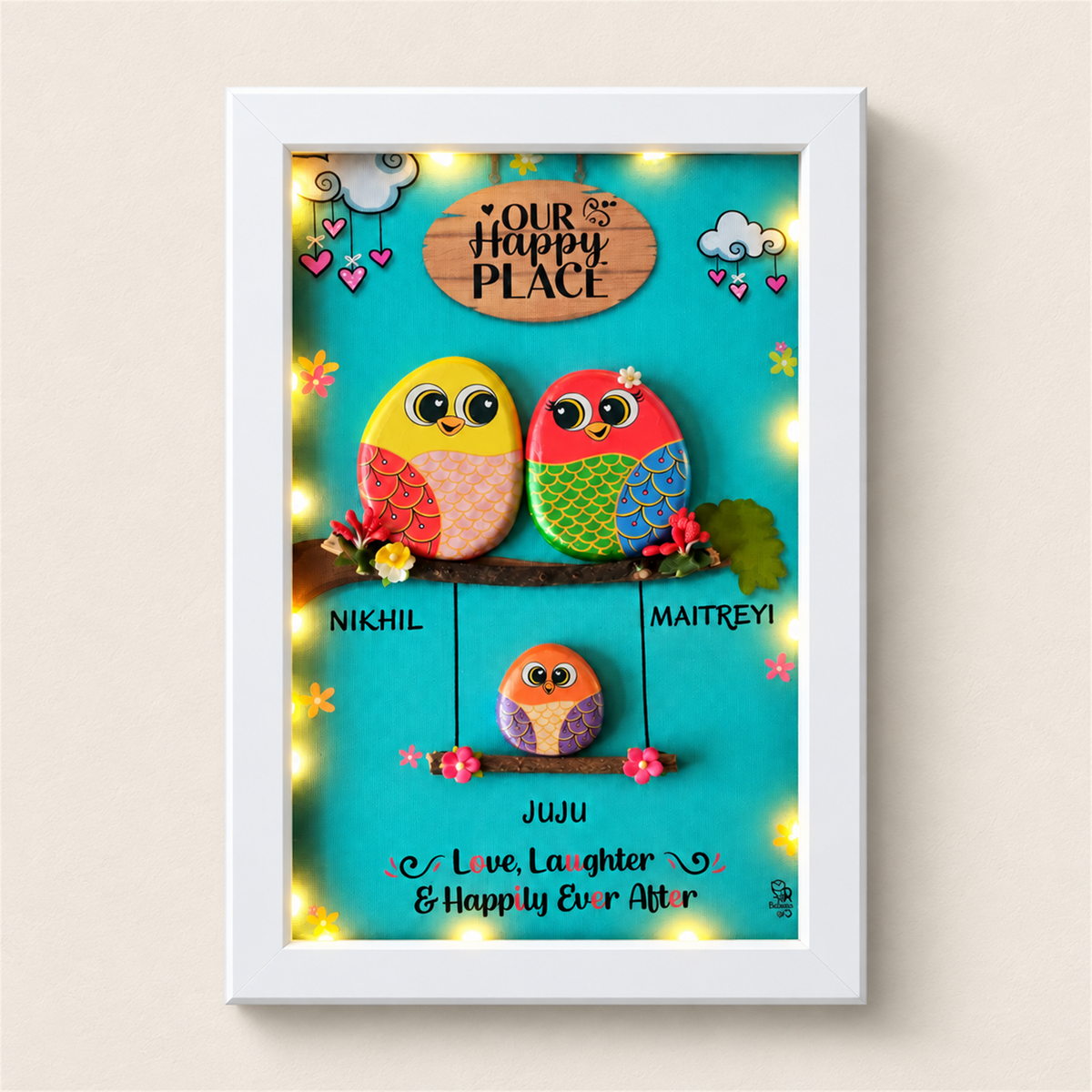 Family Joyful Nest Pebble Art: two birds above a smaller bird on a swing against a turquoise background, white frame, on a beige background