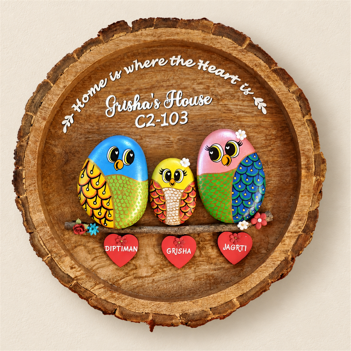 Lively Family Pebble Art: three colourful birds on a round wooden plaque with heart-shaped name tags, on a beige background